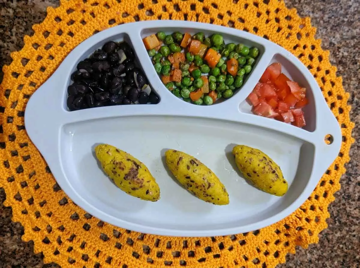 Prato com divisórias de bebê de 11 meses com feijão preto, ervilha com cenoura, tomate picado e bolinhos assados