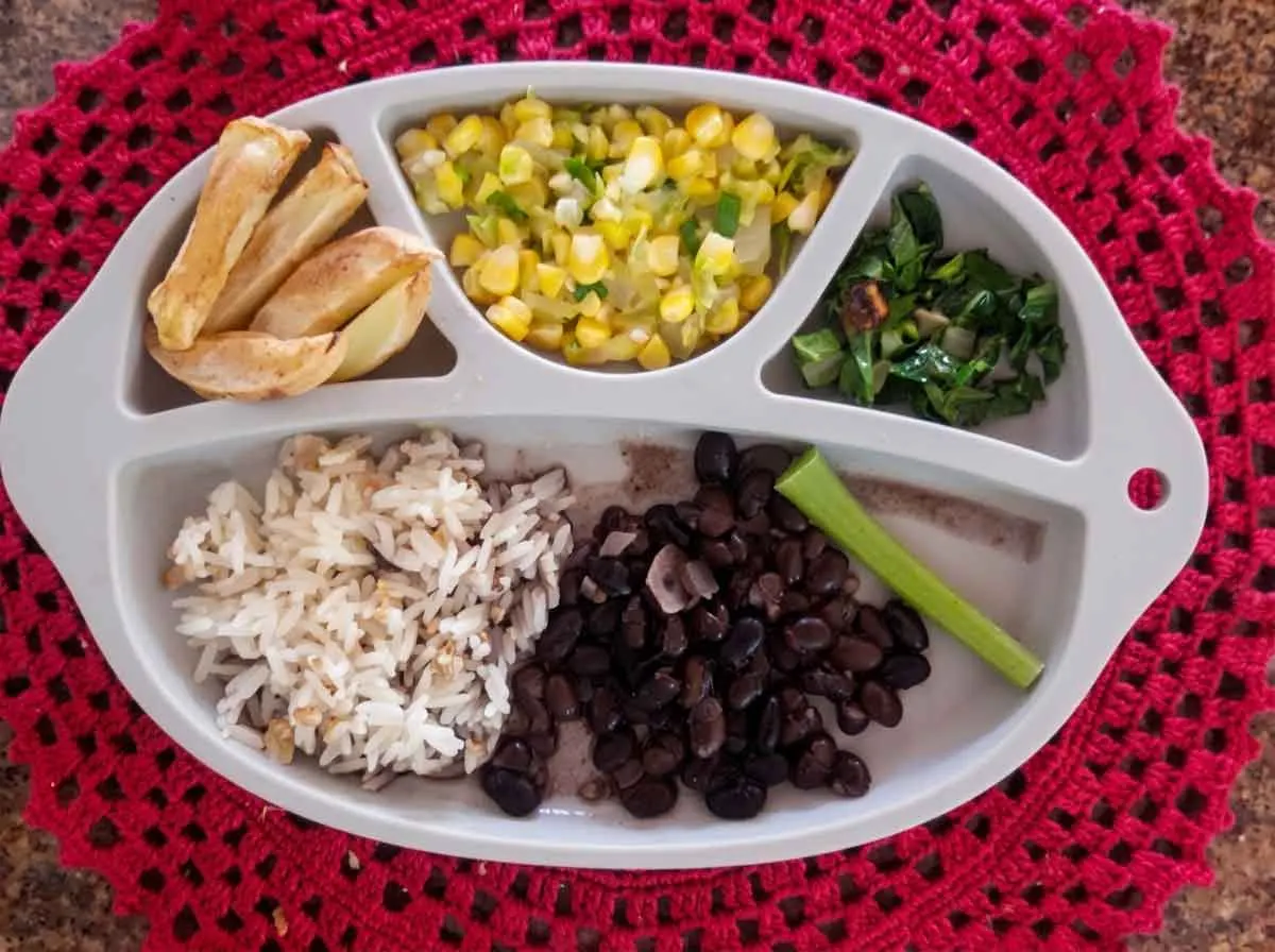 Prato com divisórias de bebê de 9 meses com arroz, feijão preto, milho refogado, couve e batata em gomos